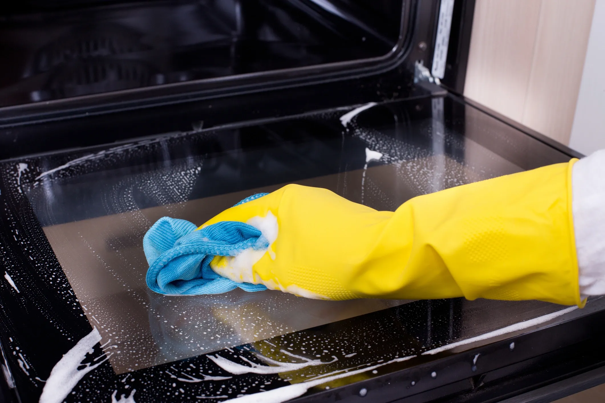 Oven cleaning with yellow gloves and blue cloth