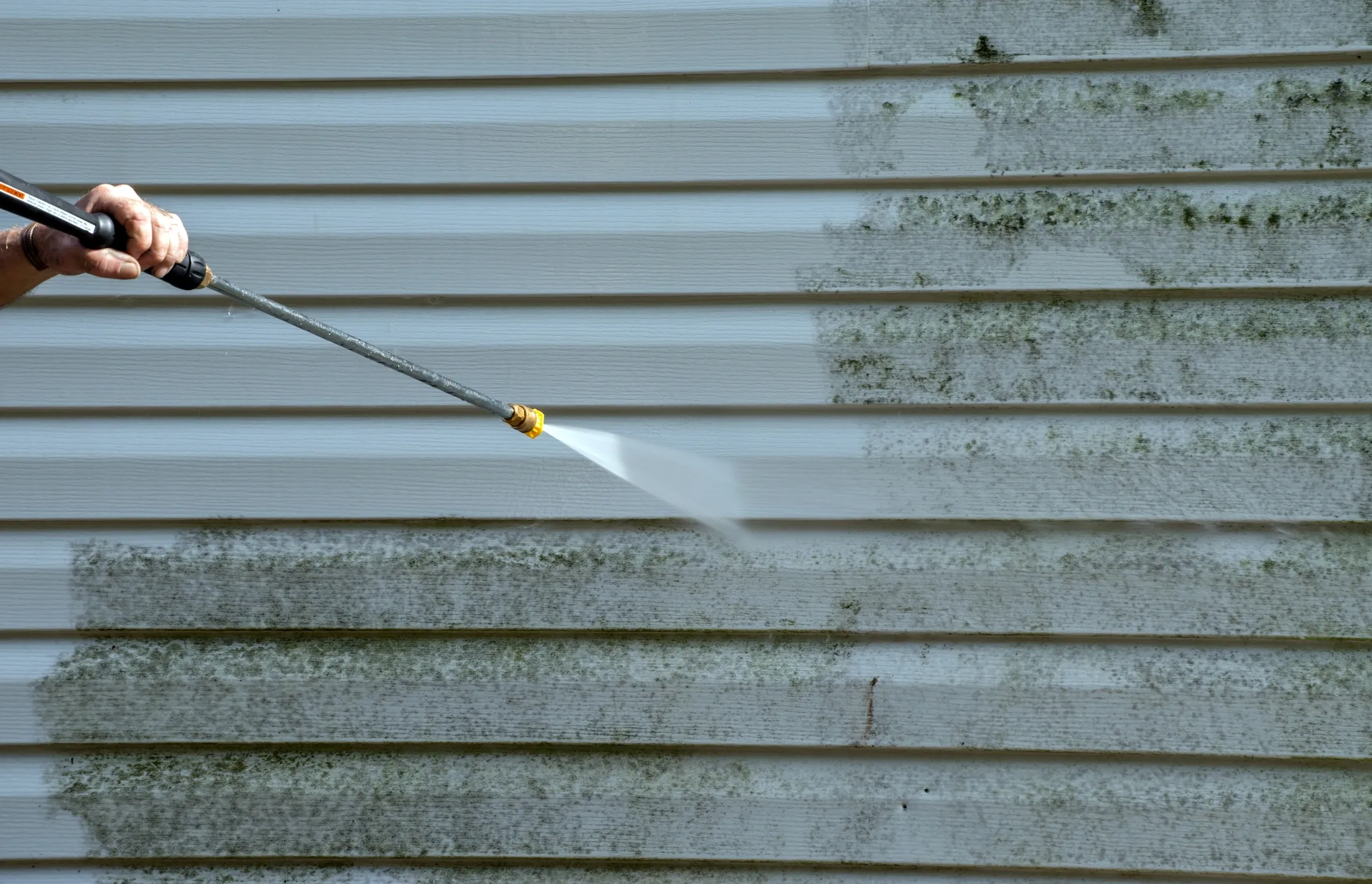 Person pressure washing mouldy siding on a residential property
