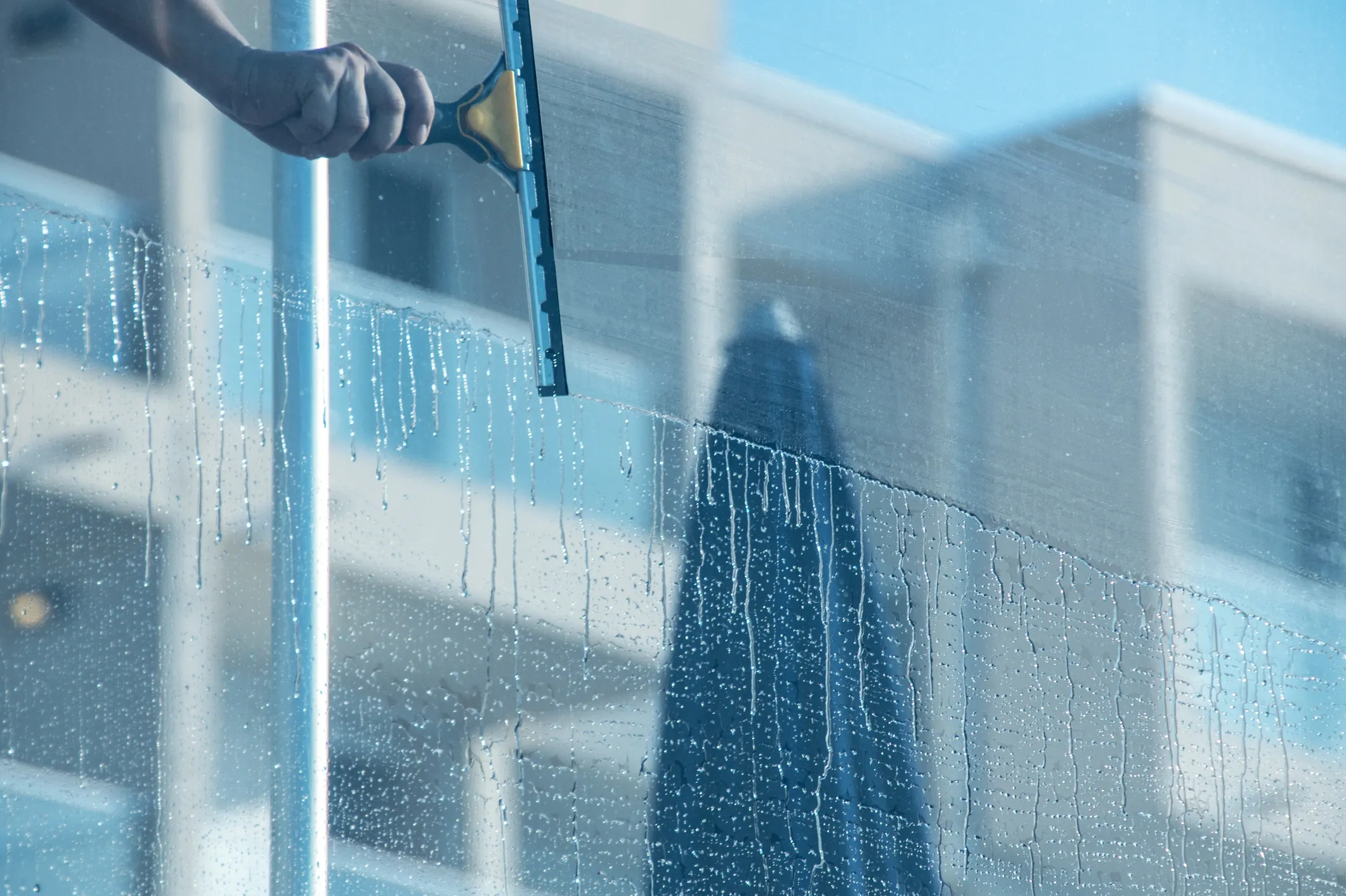 Person cleaning a high-rise window with a squeegee during a professional window cleaning service