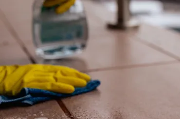 Gloved hand wiping tile floor with cloth and spray bottle