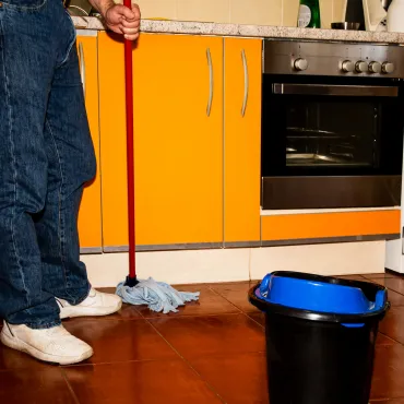 Kitchen floor mopping with mop and bucket — bright orange cabinetry