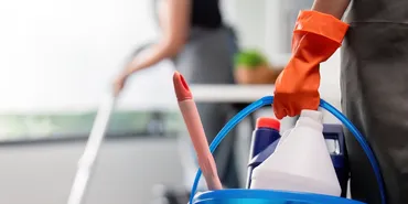 Cleaner holding bucket of supplies with vacuum in background
